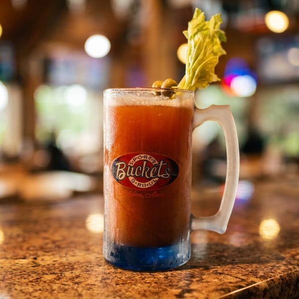 A frosty mug of Bloody Mary with celery and olives on a granite bar top.