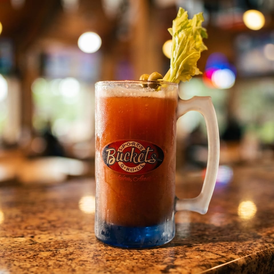 A frosty mug of Bloody Mary with celery and olives on a granite bar top.