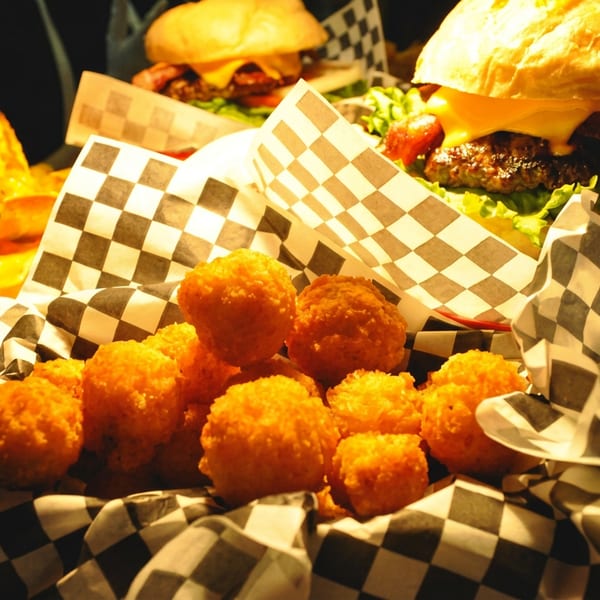 A basket of golden fried hush puppies, nachos, and two cheeseburgers with bacon and lettuce.