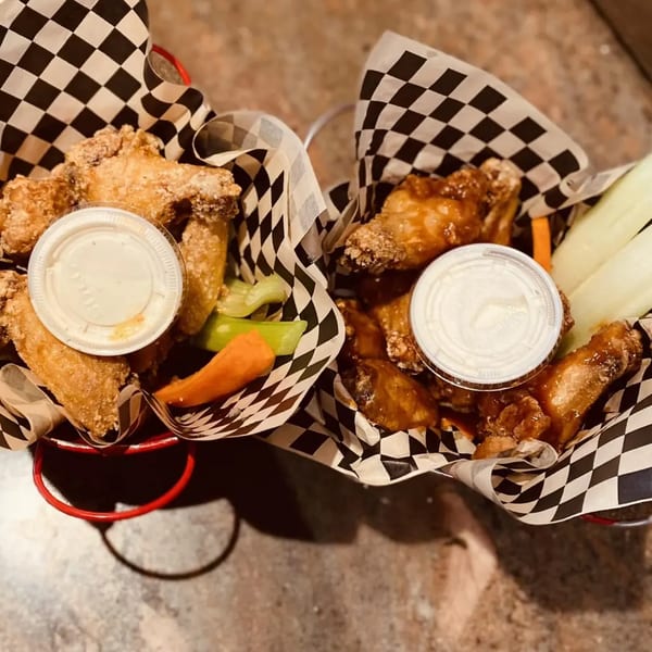 Two buckets of chicken wings, one plain and one sauced, with dipping sauce and vegetables.