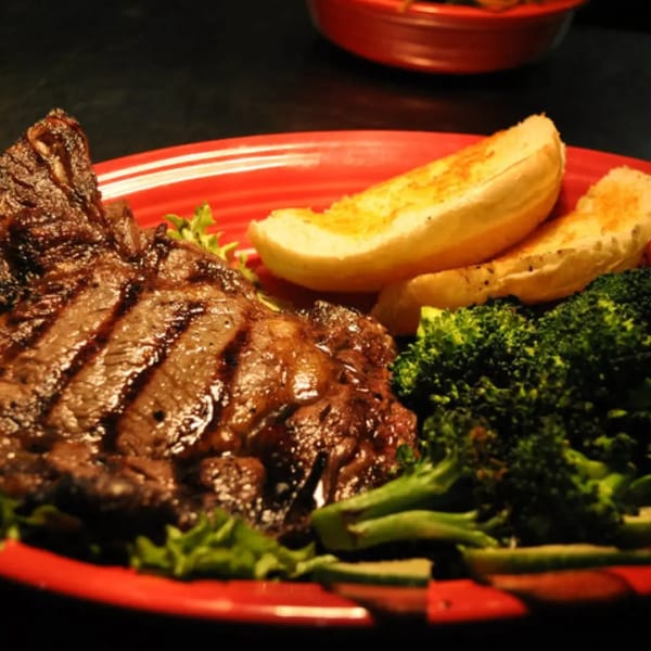 Grilled steak with grill marks, served on a red plate with broccoli, lettuce, and garlic bread.